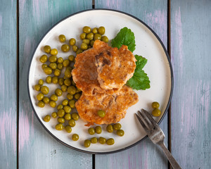 Delicious fishcakes with green peas for a light breakfast, fork lying on a wooden rustic tray