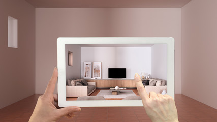 Augmented reality concept. Hand holding tablet with AR application used to simulate furniture and design products in empty interior with terracotta tiles floor, cosy living room