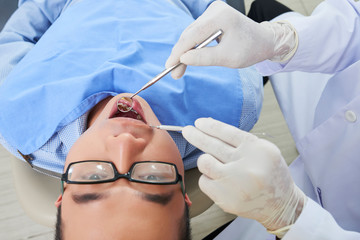 Asian man wearing eyeglasses getting regular dental exam in clinic horizontal close up from above shot