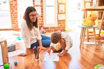 Beautiful teacher and toddler drawing using pencils and paper around lots of toys at kindergarten