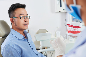 Horizontal portrait of serious Asian man wearing eyeglasses having consultation at modern dentist's office