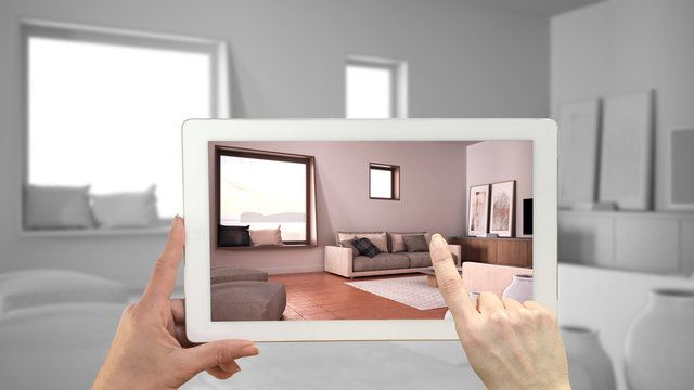 Augmented reality concept. Hand holding tablet with AR application used to simulate furniture and design products in total white unfinished background, cosy living room