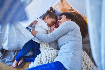Young beautiful teacher and toddler smiling with happy face lying down over blanket inside tipi at...