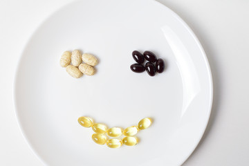 Astaxanthin, multivitamins and fish oil in a shape of smile on a white plate.