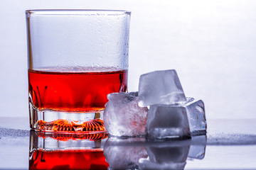 Glass of whiskey and ice on a glass table.