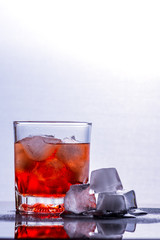 Glass of whiskey and ice on a glass table.