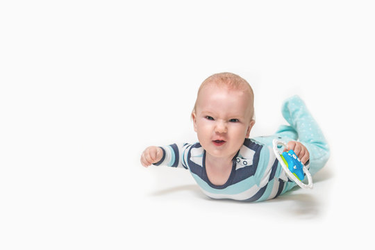 Grinning baby boy is lying on white background holding a toy. Photo contains a lot of free space for your use. All potential trademarks are removed. 
