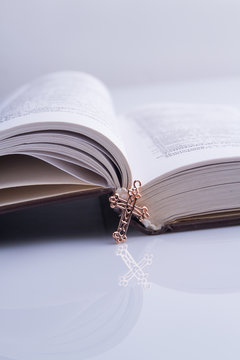 New opened holy bible and shiny golden cross. Cropped image. White background.