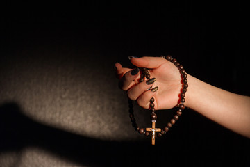 Woman's hand holding a christian cross. Symbol of faith. Black background.