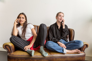 Two Women Seated on Leather Love Seat Talking on Phones