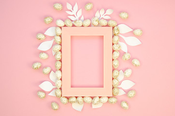 Pink plastic Easter frame decorated with papercraft leaves and Easter eggs. Mockup with copy space for text on a pastel pink background