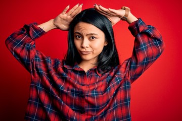 Young beautiful chinese woman wearing casual shirt over isolated red background Doing bunny ears gesture with hands palms looking cynical and skeptical. Easter rabbit concept.
