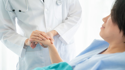 Medicine,health care and trust concept.Doctor holds the hand of a patient as a sign of care and consolation.Hand of doctor reassuring his female patient in bed at hospital.