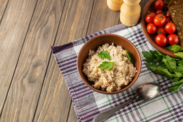 Healthy vegetarian breakfast with wheat porridge in a bowl, bread, tomatoes and parsley on wooden rustic table.