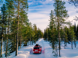 Red car with roof rack driving on snow forest road in winter