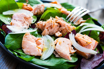 Salmon salad - roasted salmon and vegetable leaves on black stone background