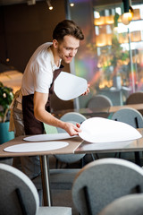Handsome waiter lays the table in cafe