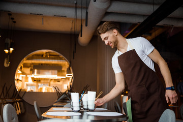 Young atrractive waiter lays the table in cafe