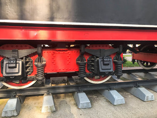 Large iron wheels of a red and black train standing on rails and suspension elements with springs of an old industrial steam locomotive