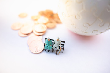 Miniature people: Old couple figure sitting long chair with stack of coins using as background retirement planning concept.