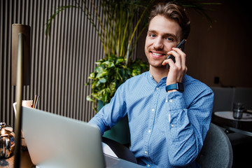 Handsome man in blue shirt working on laptop computer in cafe