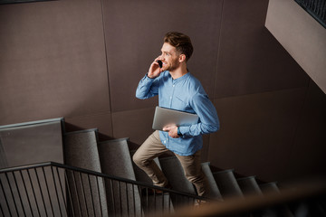 Fototapeta premium Handsome Caucasian guy with laptop walking on stairs