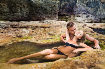 Young happy beautiful couple woman and man enjoying time in natural rock pool with water with rocks wall at background on clear summer day. Travelling, vacations, romantic weekend, honeymoon concept