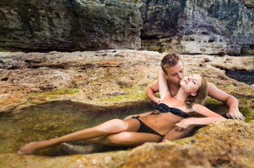 Obraz premium Young happy beautiful couple woman and man enjoying time in natural rock pool with water with rocks wall at background on clear summer day. Travelling, vacations, romantic weekend, honeymoon concept