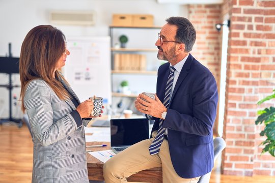 Two middle age business workers smiling happy and confident. Speaking with smile on face drinking coffe at the office