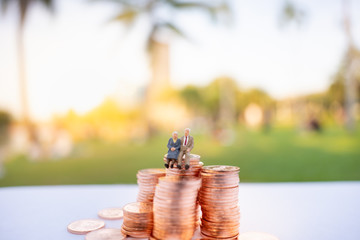 Miniature people: Old couple figure sitting on stack of coins using as background retirement planning concept.
