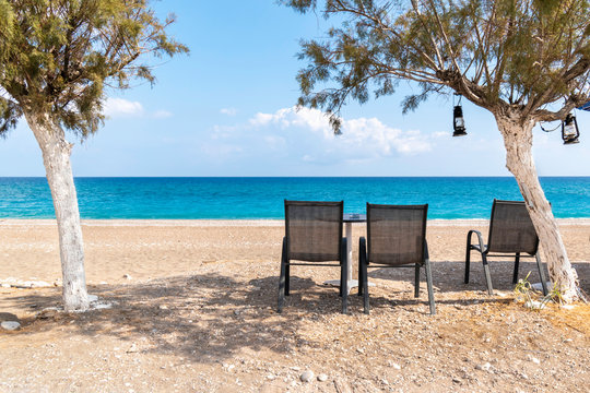 Empty chairs under tree with view of sea on Afandou beach near Faliraki (Rhodes, Greece)