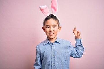 Young little boy kid wearing easter bunny ears over isolated pink background smiling with happy...