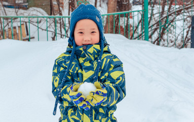 Cute Asian baby boy playing on snowfall white snow, sculpting snowballs with a toy snowball maker. Winter sport. We play in the Park in the fresh air. With a smile of happiness.