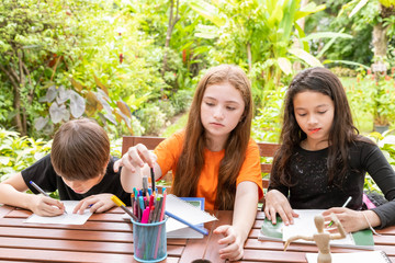 Children, boy and girl, doing homework and drawing together in garden at home.