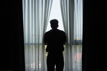 Silhouette of man standing at the window in the dark room. Man thinking and motivational concept