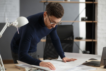 Fototapeta na wymiar Architect working in office with blueprints.Engineer inspect architectural plan, sketching a construction project.Portrait of handsome bearded man sitting at workplace. Business construction concept.