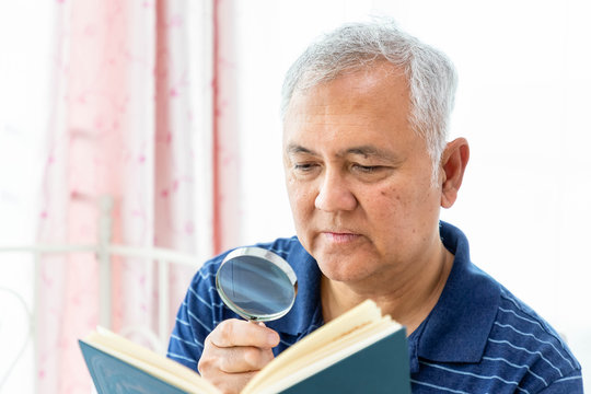 Happy elderly senior man male enjoy reading book using magnifying glass