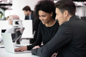Happy multiracial colleagues managing project on laptop at workplace.