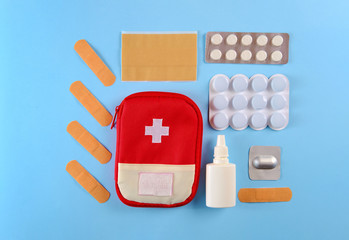 Closed tourist first aid kit pouch near to the pills, adhesive bandages and nasal spray on the bright blue background