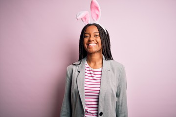 Young african american girl wearing cute easter bunny ears over pink background with a happy and cool smile on face. Lucky person.