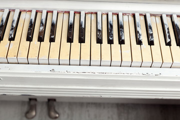 The black and white keys of the old piano are covered in white paint and dust. A vintage photograph was taken indoors after renovation under artificial lighting.