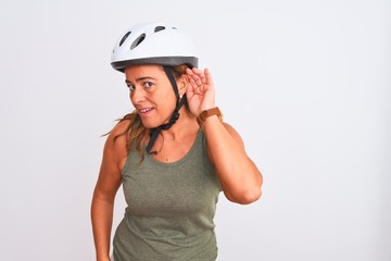 Middle age mature cyclist woman wearing safety helmet over isolated background smiling with hand over ear listening an hearing to rumor or gossip. Deafness concept.