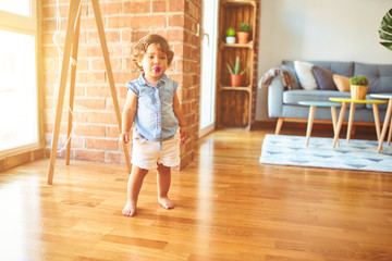 Beautiful toddler child girl wearing blue denim shirt standing on the floor using pacifier