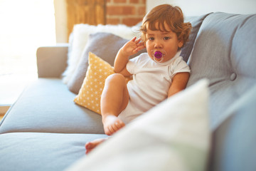 Beautiful toddler child girl wearing white t-shirt sitting on the sofa using pacifier
