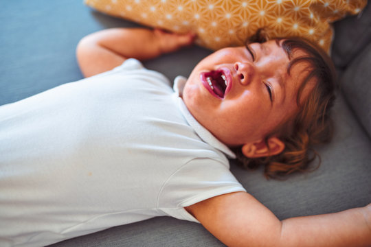 Beautiful toddler child girl wearing white bodysuit crying lying down on the sofa