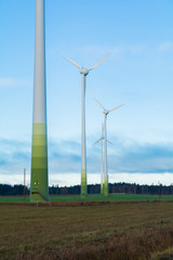Fototapeta premium Wind electricity generator park, visible green farming fields, trees, grass and blue skies with clouds
