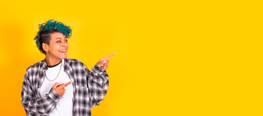 young african american woman with blue curly hair pointing at yellow background