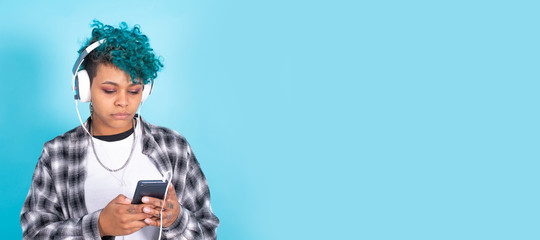 young african american woman with mobile phone and headphones isolated on blue background