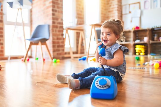 Beautiful toddler sitting on the floor playing with vintage phone at kindergarten