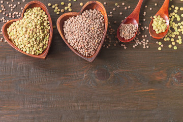 two wooden bowls with red and green raw lentils on a wooden background top view. grains of red and green lentils in bowls and spoons on a wooden background top view.